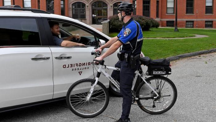 A police officer on a bicycle talks to a College employee in a van